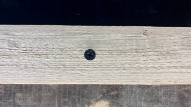 Siyah kendi kendine dokunan vidalar ve eski bir atölye masasında bir tornavida. Kendini beceren bir vida tahta bir bloğa vidalanır.