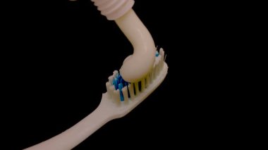 Beyaz diş macunu siyah arka planda bir diş gagasına yayılır.