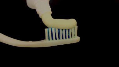 Beyaz diş macunu siyah arka planda bir diş gagasına yayılır.