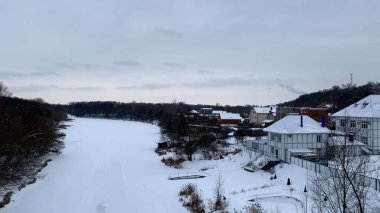 Yapraksız kış manzarası, karanlık bir gökyüzü köprüsü altında donmuş bir nehir ve bir sürü kar.
