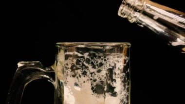 Tezgahtaki barmen siyah arka plandaki bir müşteri için şişeden bardağa light bira dolduruyor.