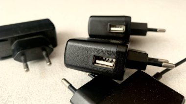 Elektrik cihazları, siyah kablolar, konnektörler ve pil paketleri için farklı şarj türleri beyaz bir masa üzerinde yatar