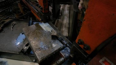 Atölyedeki usta metal için testereyle çalışıyor, makine bıçağı soğutmak için sabunlu su kullanarak çelik profili herhangi bir açıdan kesiyor.