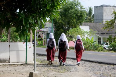 Lampung, Endonezya, 17 Aralık 2021 İlköğretim Okulu öğrencileri okula sırtlarında çantalarla, Endonezya 'nın Lampung köyünde bir köyde yürüyerek giderler.