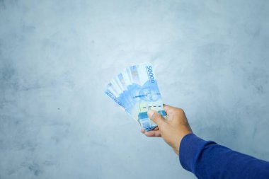 Asyalı adam rupiah banknotlarını tutuyor ve gösteriyor.