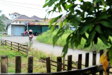 Lampung, Endonezya, 11 Mart 2022: Sokakta bisikletle gezen ve mallarını öğleden sonra satan yetişkin bir kadın üzerine seçici bir odaklanma. Bu fotoğraf gürültü ve tahıl içeriyor..