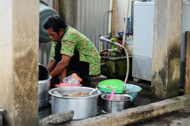 Lampung, Endonezya, 11 Mart 2022: Evinin arkasında bulaşık yıkayan yetişkin bir adama odaklanın. Bu fotoğraf gürültü ve tahıl içeriyor..