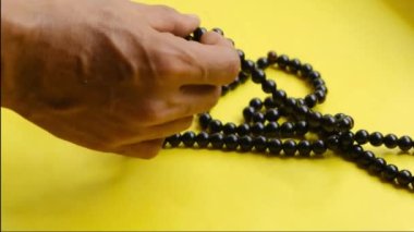Boncuklarla dua okuyan bir adam, sarı arka planda İslami dini simgeler.