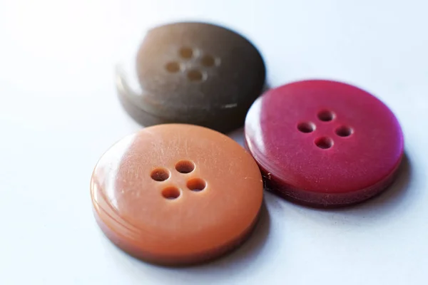 Three colourful sewing buttons for clothes are isolated on a red background.