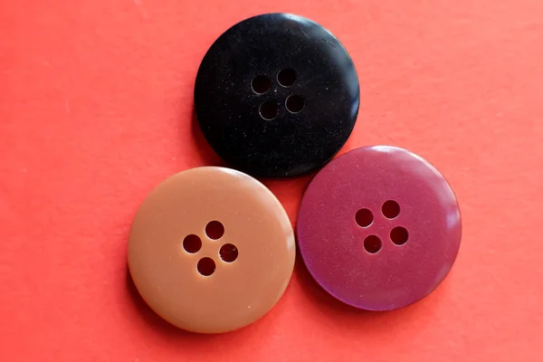 Three colourful sewing buttons for clothes are isolated on a red background.