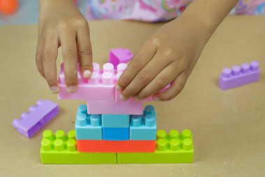 Küçük kızın elleri masanın üzerinde oyuncak bloğu parçalayarak oynuyor. Stüdyo çekimi.