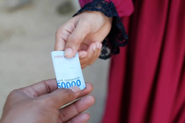 Bir kadının eli bir erkeğin eline rupiah banknotları verir.
