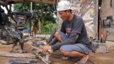 Lampung, Endonezya, 22 Nisan 2022: Motosiklet tamir atölyesindeki kıvılcımlarla metal boruları öğüten ve parlatan adam