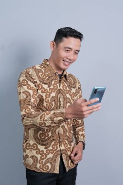 Asyalı adam ifadesi elinde akıllı telefon, batik gömlek giyiyor.