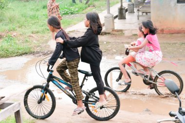 Lampung, Endonezya 20 Haziran 2022: Çocuklar yağmurdan sonra sulak ve çamurlu yollarda bisiklet sürüyorlar