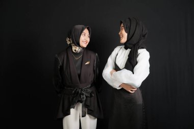 Two happy young Asian Muslim women interact isolated on black background.