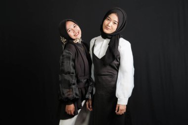 Two happy young Asian Muslim women interact isolated on black background.