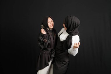 Two happy young Asian Muslim women interact isolated on black background.