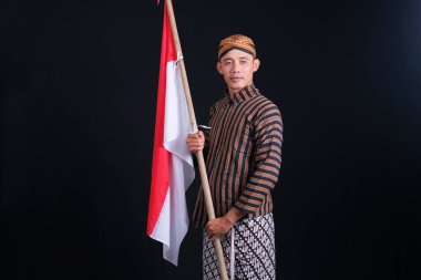 Man wearing Javanese traditional clothes holding Indonesian national flag in Indonesia's independence month, studio shoot