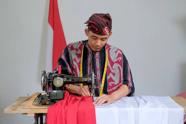 A young tailor in traditional woven clothes is busy making the Indonesian national flag ahead of independence day