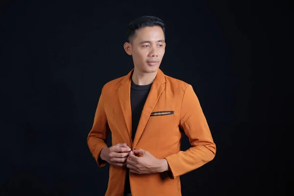 Young businessman in orange suit holding shirt button isolated on black background