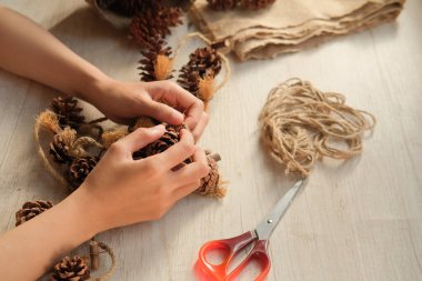 Part of a woman's hands making wall hangings from pinecones and jute rope