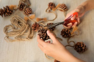 Part of a woman's hands making wall hangings from pinecones and jute rope