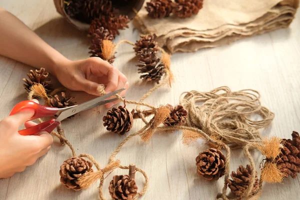 Part of a woman's hands making wall hangings from pinecones and jute rope