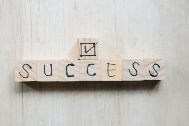 Wooden cube with the text SUCCESS, The word is written on a wooden cube standing on a textured surface.