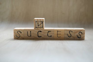 Wooden cube with the text SUCCESS, The word is written on a wooden cube standing on a textured surface.
