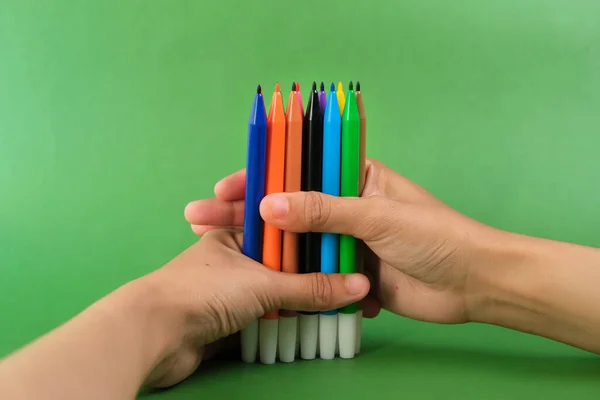 Human hand holding bunch of colorful markers on green background. Concept of creativity, drawing, bright world