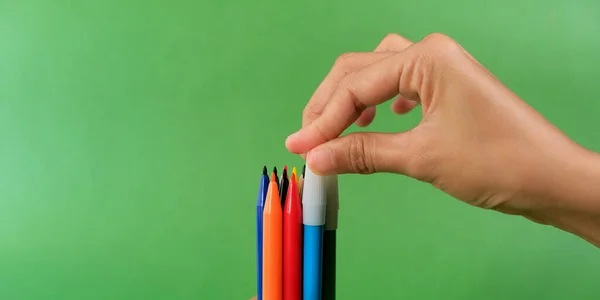 Human hand holding bunch of colorful markers on green background. Concept of creativity, drawing, bright world