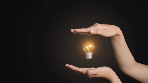 A person's hand with a floating light bulb shone brightly above his hand. Concept image of business idea with copy space for text.