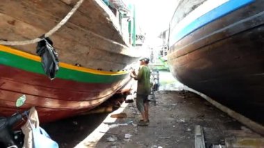Bir zanaatkar gemi bakımı için rıhtımda öğütücüyle gövdenin yüzeyini düzleştirir ve gövdeyi boyar.
