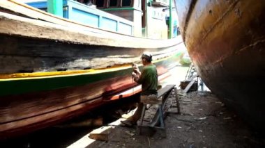 Bir zanaatkar gemi bakımı için rıhtımda öğütücüyle gövdenin yüzeyini düzleştirir ve gövdeyi boyar.