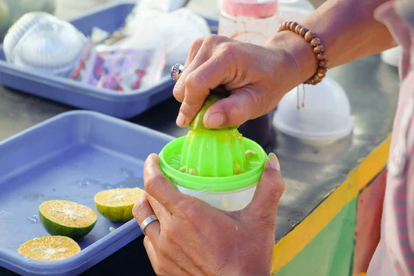 A hand squeezes juice from an orange on a manual plastic squeezer. Man selling juice squeezing fresh citrus fruit. Side view