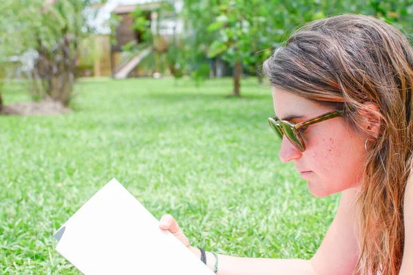 靠近一个年轻的高加索女人 她正在阅读一本躺在草地上的书 横向的 有复制空间 — 图库照片