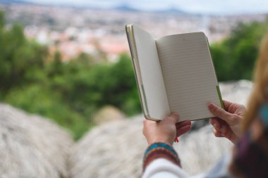 Beyaz kadın elleri arka planda şehir manzaralı boş bir defter tutuyor. Yatay olarak. Kopyalama alanı ile.