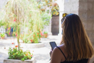 Bir manastırın içinde cep telefonunu kontrol eden beyaz bir kadının arka görüntüsü. Yatay olarak. Kopyalama alanı ile.