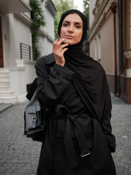 Snygg muslimsk kvinna med hijab promenader och röker cigaretter på gatan — Stockfoto