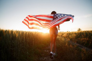 4 Temmuz. 4 Temmuz 'da. Gururlu bir kadın günbatımında Amerika bayrağını güzel bir simgeye taşıyor. Bağımsızlık Günü, Amerikan ulusal vatanseverlik bayramı, demokrasi ve gazi saygı konsepti.