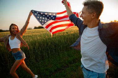 4 Temmuz. 4 Temmuz 'da. Gururlu çift gün batımında Amerika bayrağını güzel bir yere taşıyor. Bağımsızlık Günü, Amerikan ulusal vatanseverlik bayramı, demokrasi ve gazi saygı konsepti.