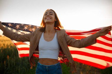 4 Temmuz. 4 Temmuz 'da. Gururlu bir kadın günbatımında Amerika bayrağını güzel bir simgeye taşıyor. Bağımsızlık Günü, Amerikan ulusal vatanseverlik bayramı, demokrasi ve gazi saygı konsepti.
