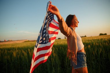 4 Temmuz. 4 Temmuz 'da. Gururlu bir kadın günbatımında Amerika bayrağını güzel bir simgeye taşıyor. Bağımsızlık Günü, Amerikan ulusal vatanseverlik bayramı, demokrasi ve gazi saygı konsepti.