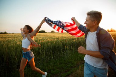 4 Temmuz. 4 Temmuz 'da. Gururlu çift gün batımında Amerika bayrağını güzel bir yere taşıyor. Bağımsızlık Günü, Amerikan ulusal vatanseverlik bayramı, demokrasi ve gazi saygı konsepti.