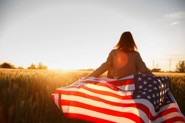 4th of July. Fourth of July. Proud woman carry USA flag against beautiful landmark on sunset. Independence Day celebrating, American national patriotic holiday, democracy and veteran respect concept