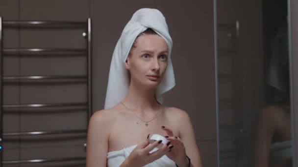 洗澡镜前 女人头上裹着毛巾 涂上润肤霜 日常晚间活动 面部清洁 剥皮美容治疗概念 — 图库视频影像