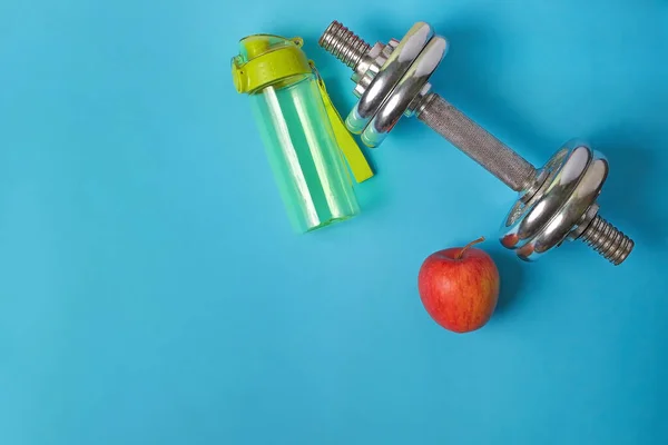 fitness background with a bottle of apple and dumbbells on a blue table