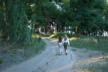 Two sisters hold hands, walk along the path into the distance. High quality photo
