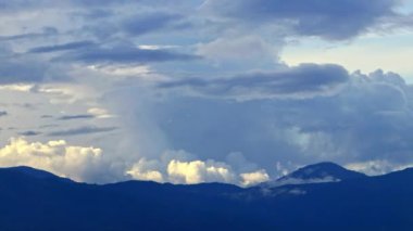 Zaman bulutları mavi dağların üzerinde kıvrılır, uzaktaki karlı zirve.